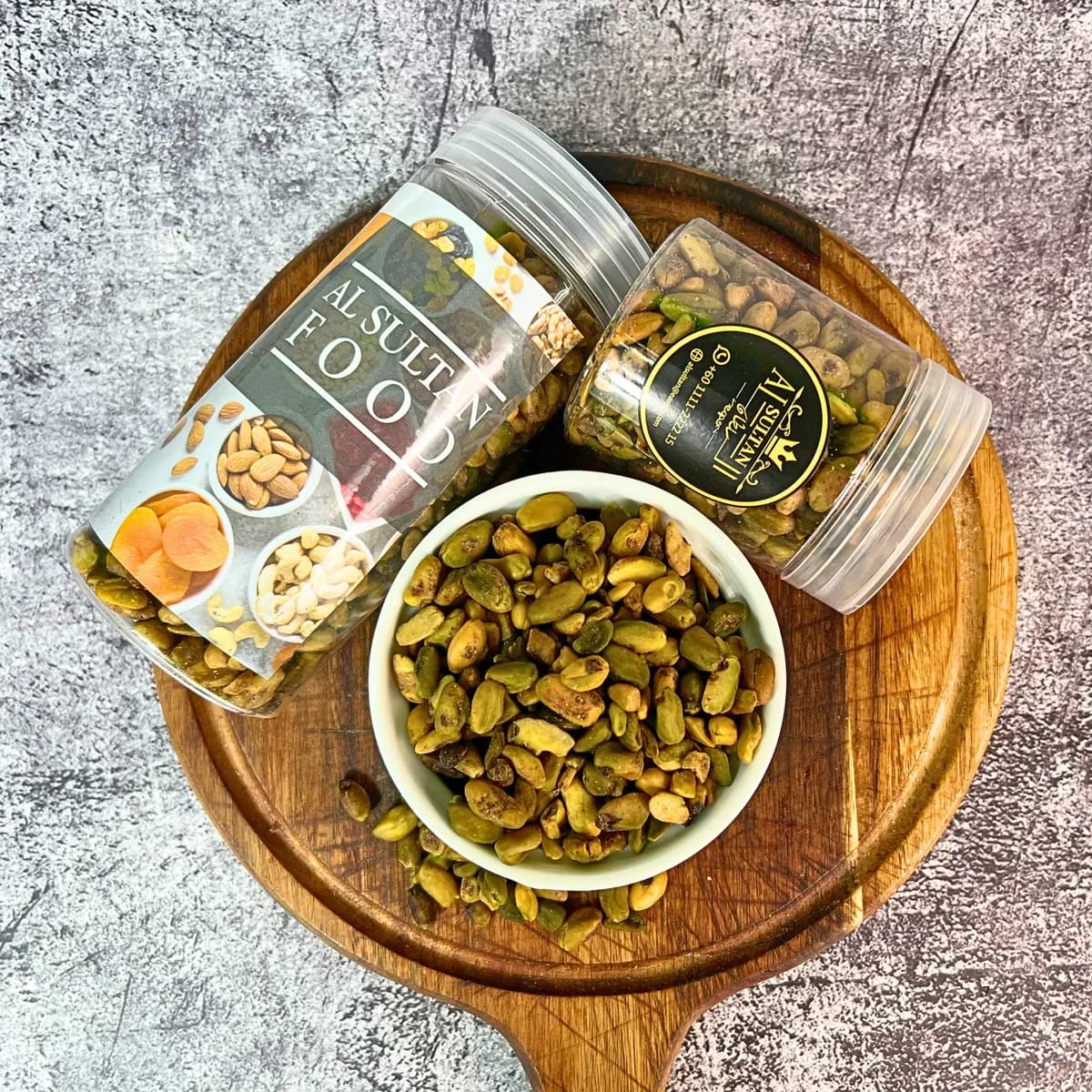 Isi pistachio mentah dalam mangkuk di atas papan kayu dengan balang AlSultanFood